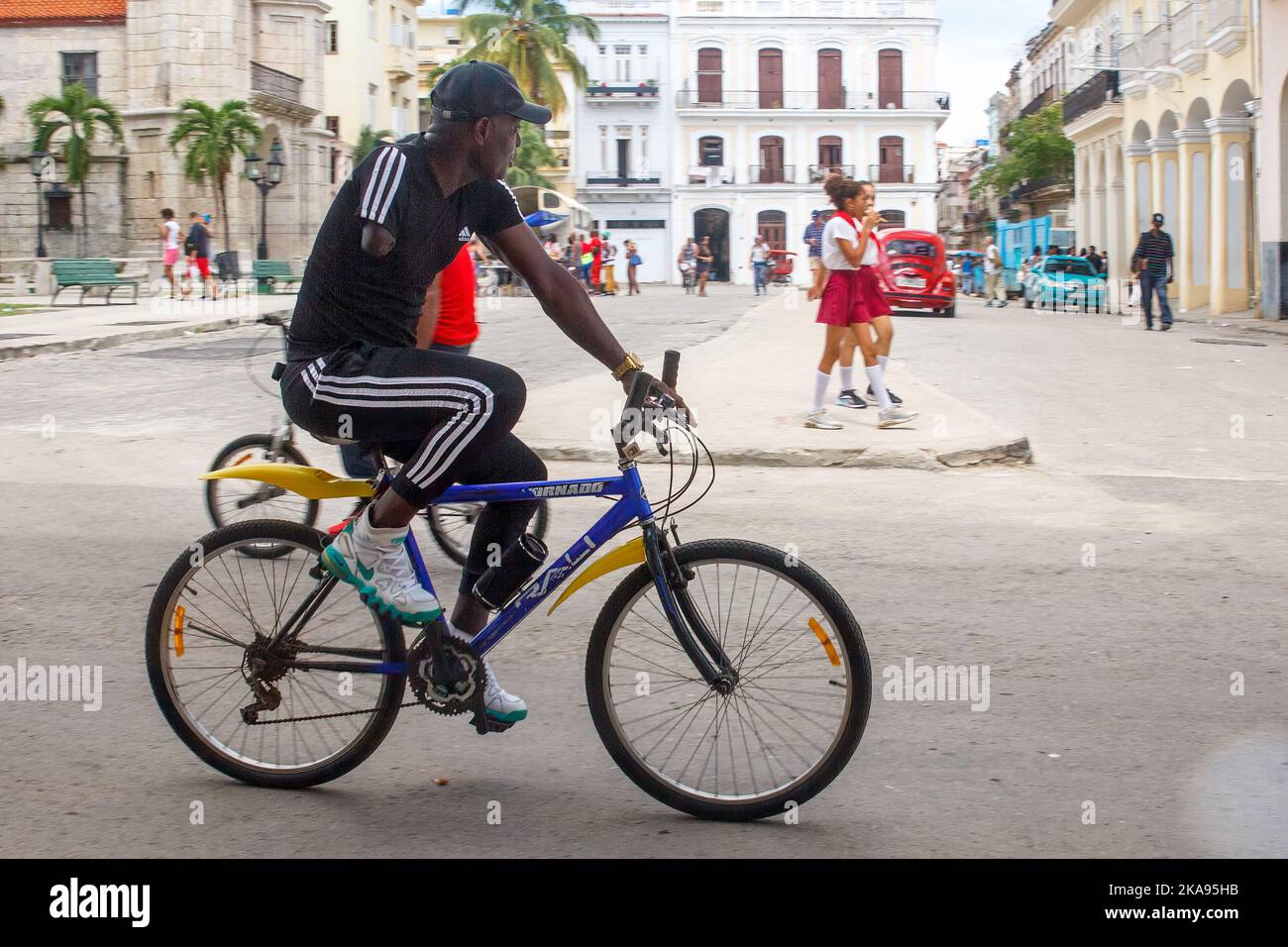 Un homme afro-caraïbe cubain vivant avec un handicap fait un vélo tandis que les étudiants pionniers en uniforme marchent en arrière-plan Banque D'Images