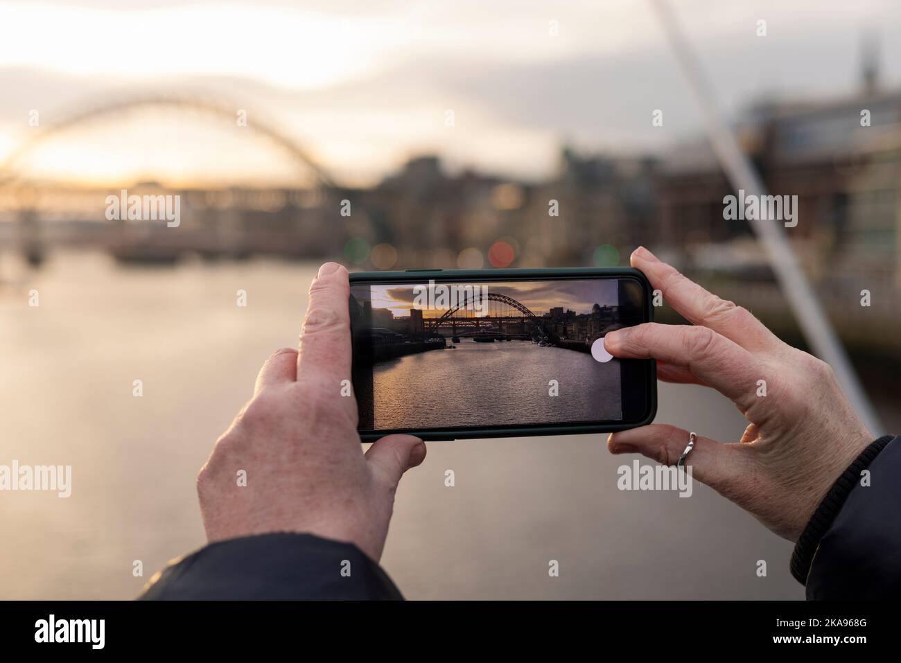 Une femme méconnaissable prenant une photo avec un téléphone portable de la rivière Tyne au crépuscule à Newcastle upon Tyne. Les ponts peuvent être vus dans la photographie Banque D'Images