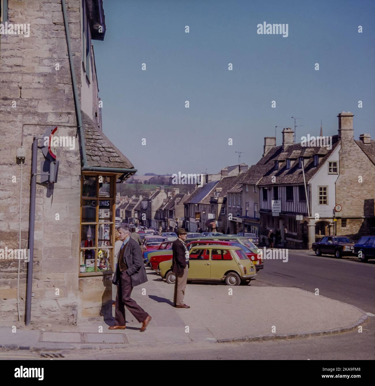 Burford High Street en 1980. Image prise de la diapositive d'origine. Burford est une ville sur la rivière Windrush, dans les collines des Cotswolds, dans le district ouest de Oxfordshire, en Angleterre. Il est souvent appelé la «porte» des Cotswolds.cette image montre les gens, les voitures et les bâtiments dans le 1980s. Banque D'Images