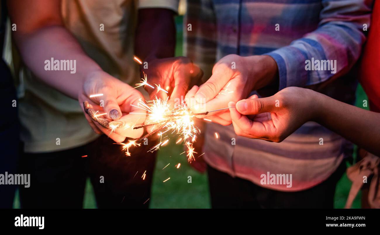 Des amis heureux qui fêtent et applaudissent avec des escroers la veille du nouvel an - se concentrer sur la main droite tenant feu d'artifice Banque D'Images