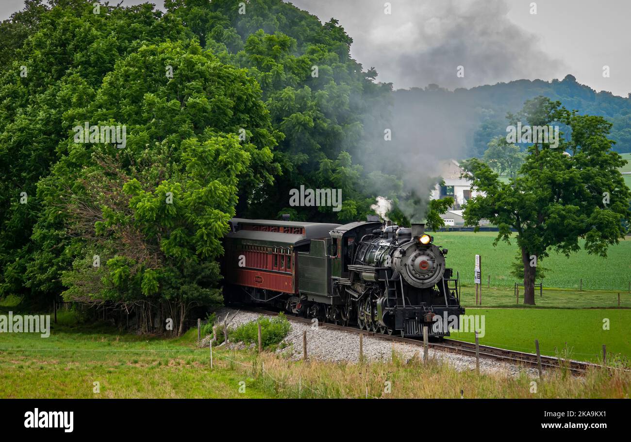 Vue sur un train de passagers à vapeur restauré qui s'approche des bois avec de la fumée et de la vapeur lors d'une journée d'été Banque D'Images