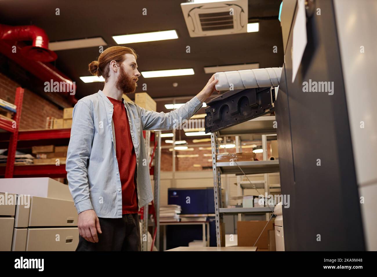Portrait d'un jeune homme qui sort un rouleau de vinyle dans une imprimerie industrielle Banque D'Images