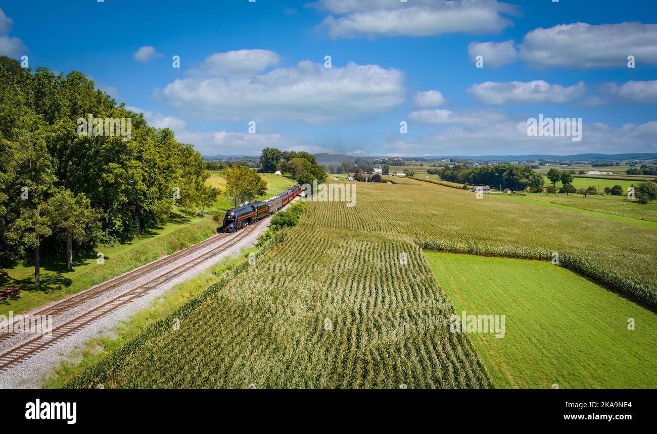 Vue de drone d'un train de passagers à vapeur approchant d'un commutateur de piste avec champs de maïs vert et terres agricoles lors d'une Sunny journée d'été Banque D'Images