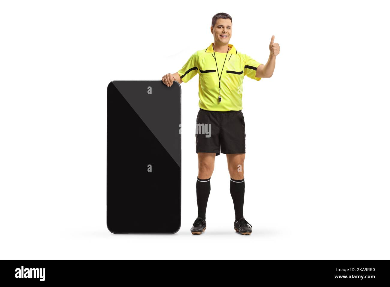 Portrait complet d'un arbitre de football debout à côté d'un grand smartphone et en faisant des gestes de pouces isolés sur fond blanc Banque D'Images