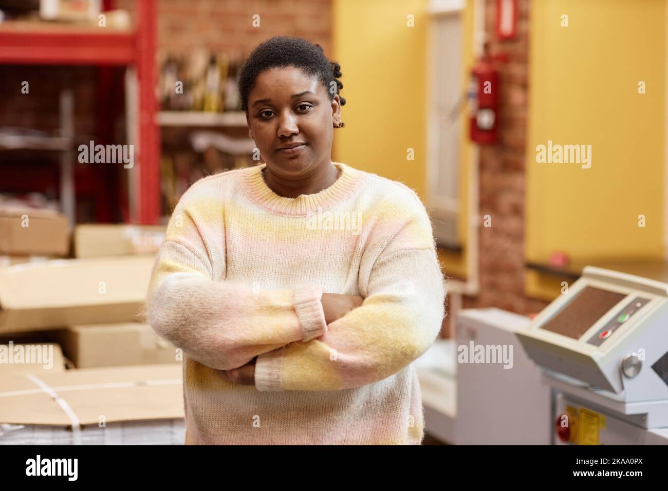Portrait à la taille haute d'une jeune femme noire travaillant dans un atelier d'impression industriel et regardant l'appareil photo tout en se tenant debout avec les bras croisés, espace de copie Banque D'Images