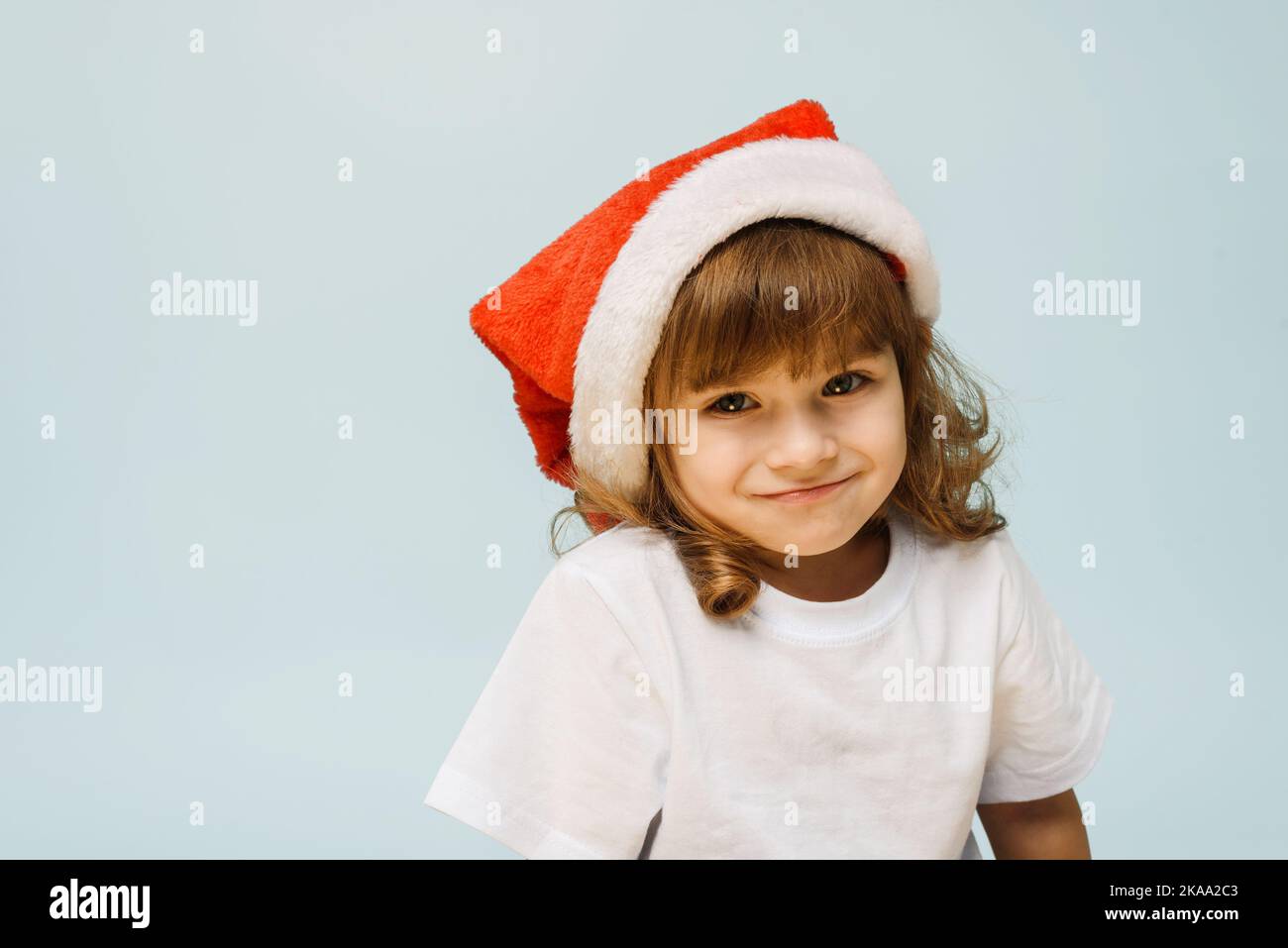 Drôle mignon fille dans un chapeau de père noël se tient sur un fond bleu avec l'espace de copie. Concept de noël et nouvel an Banque D'Images