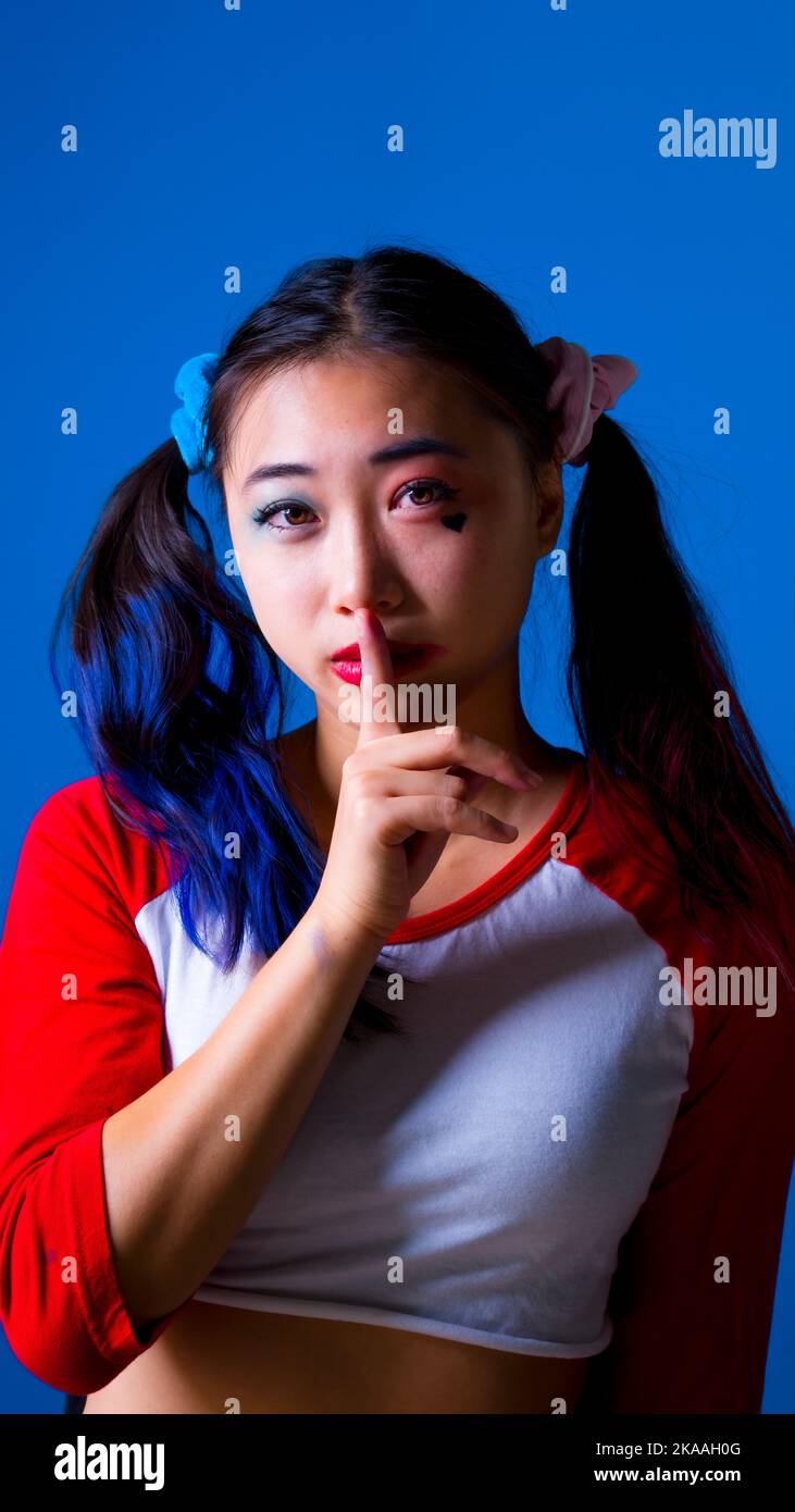 Jeune femme vêtue d'un déguisement d'Arlequin avec le doigt sur les lèvres pour dire calme | Shhh Banque D'Images