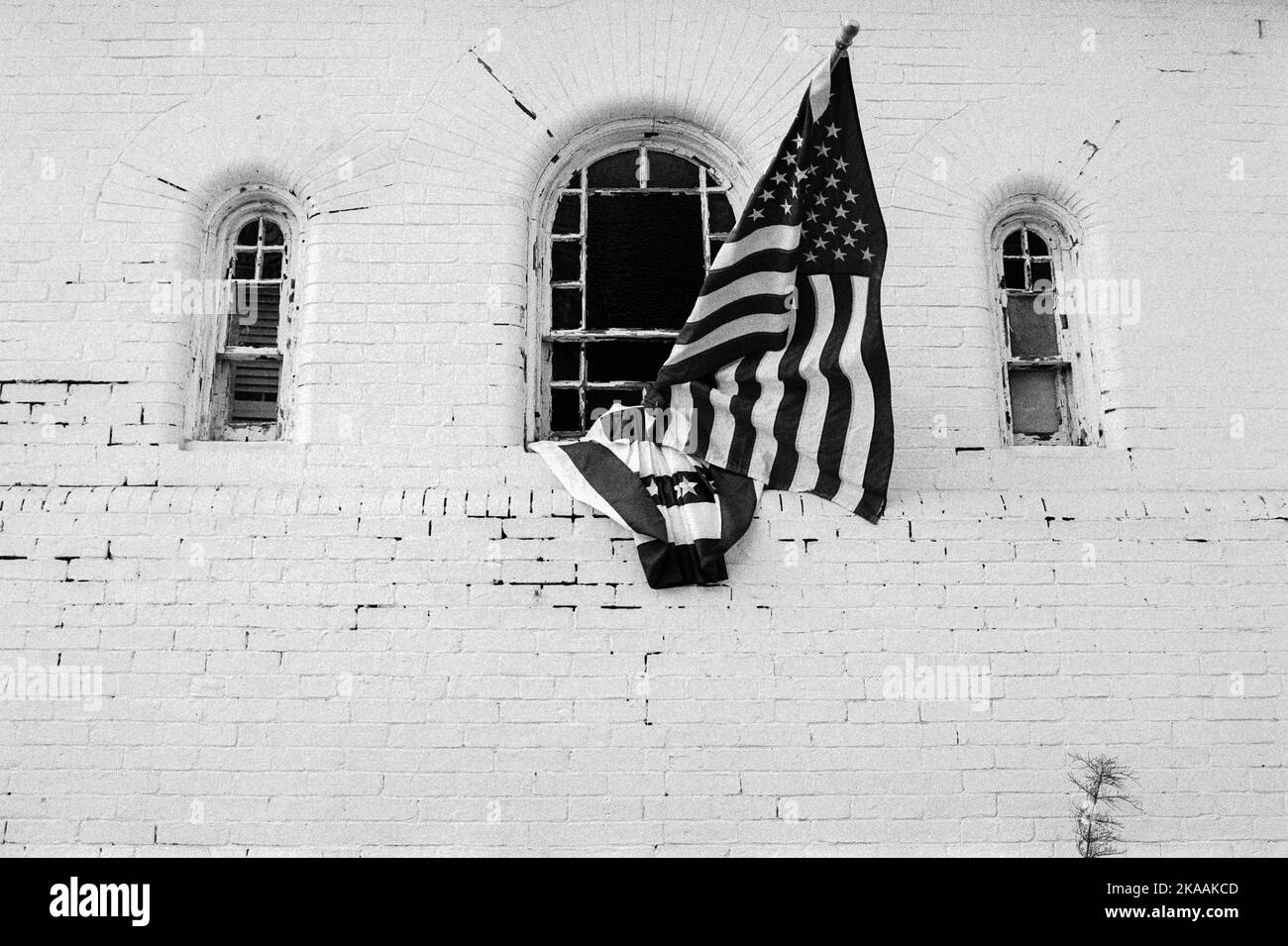 Un bâtiment en brique brute peint en blanc avec deux drapeaux américains montés sur une fenêtre à Rockport, Massachusetts. L'image a été capturée en noir analogique Banque D'Images
