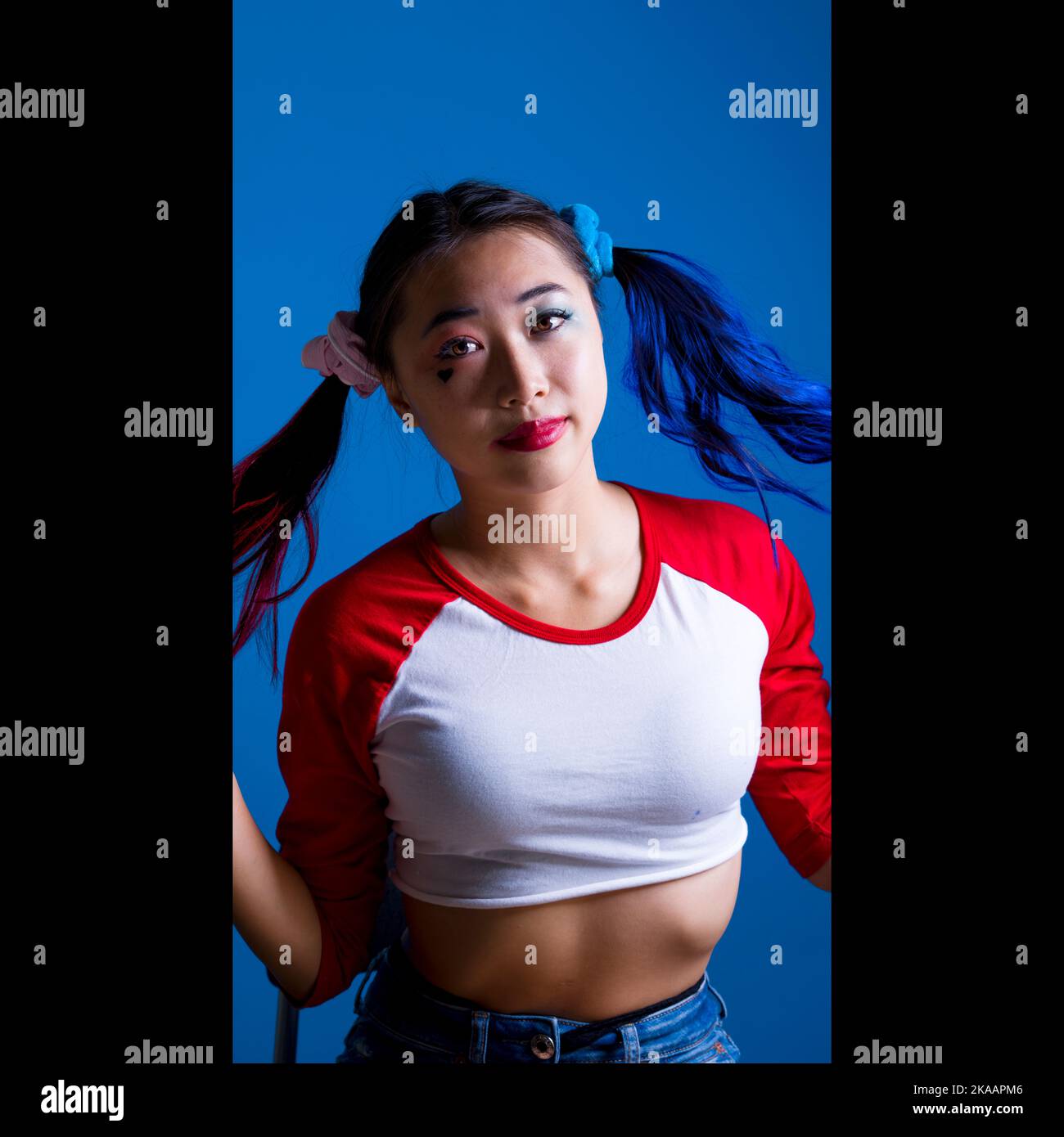 Jeune femme en maquillage d'Arlequin assise avec espace de copie en fond bleu Banque D'Images