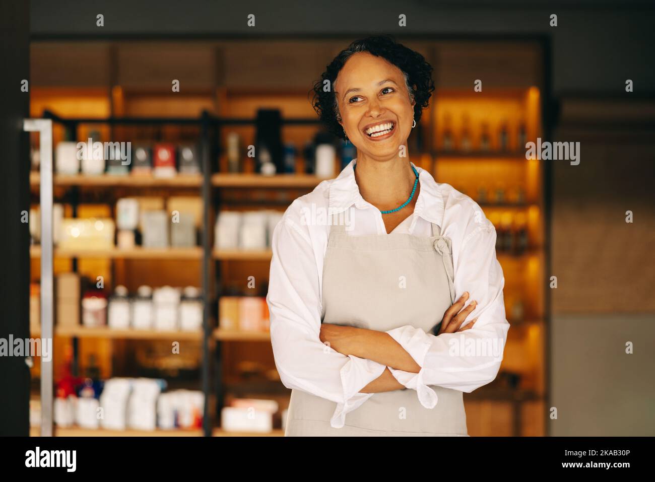 Propriétaire réussi de petite entreprise souriant joyeusement en se tenant à l'entrée de son magasin d'alimentation avec ses bras croisés. Entrepreneur mature courant Banque D'Images