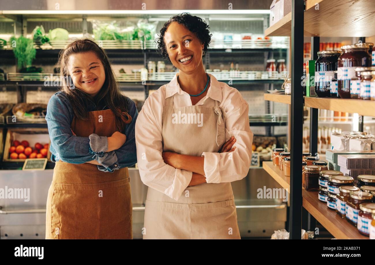 Les employés des épiceries qui ont réussi à sourire à la caméra tout en se tenant ensemble dans leur magasin. Femme heureuse avec le syndrome de Down travaillant dans un superm local Banque D'Images