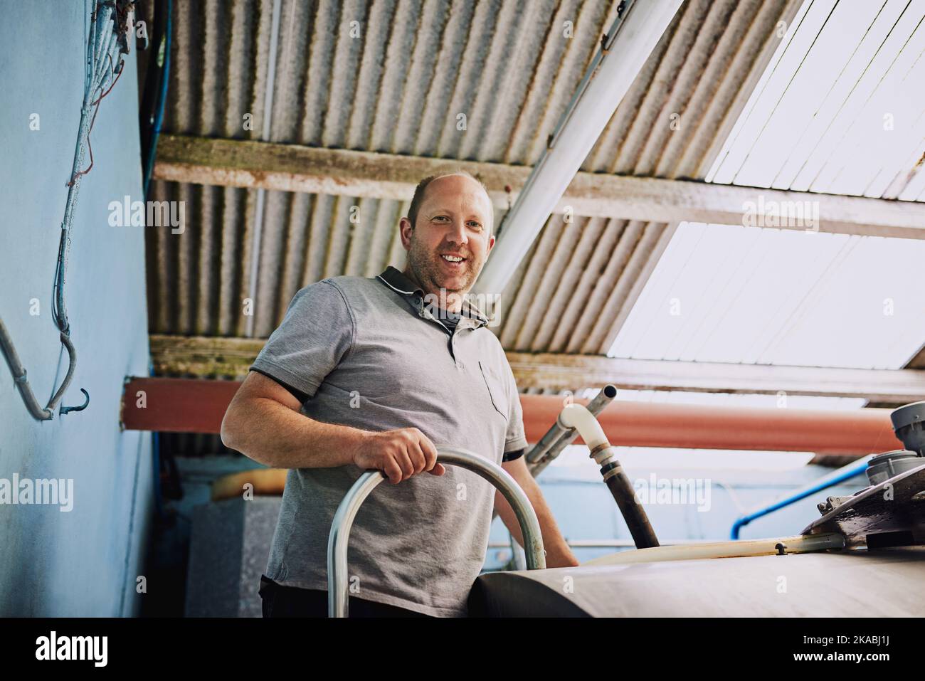 J'aime vraiment travailler sur ma ferme laitière. Portrait à angle bas d'un fermier mâle remplissant des récipients à lait dans son usine laitière. Banque D'Images