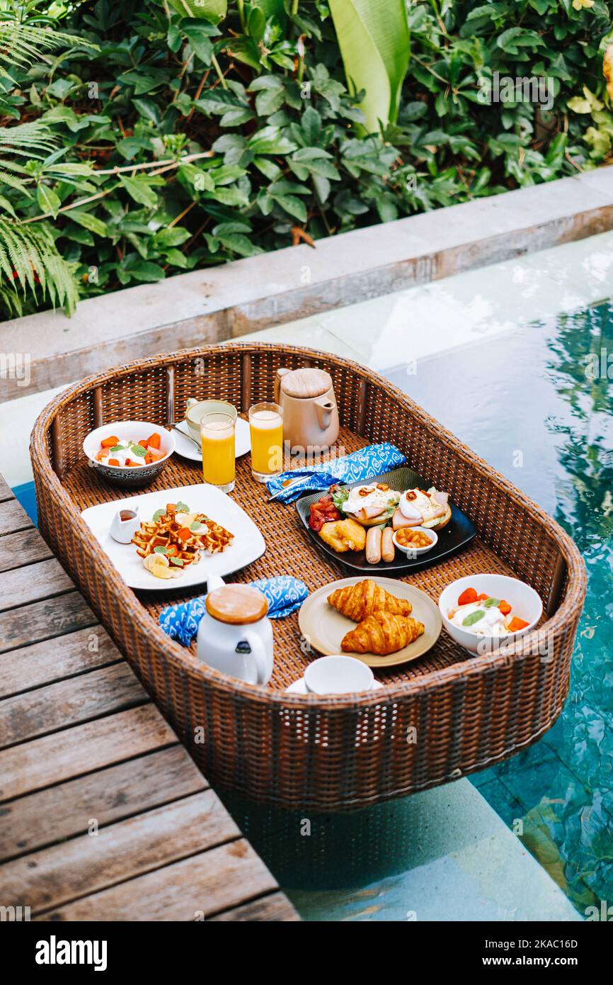 Le plateau de petit-déjeuner en rotin synthétique ou en bambou flotte au coin de la piscine Banque D'Images