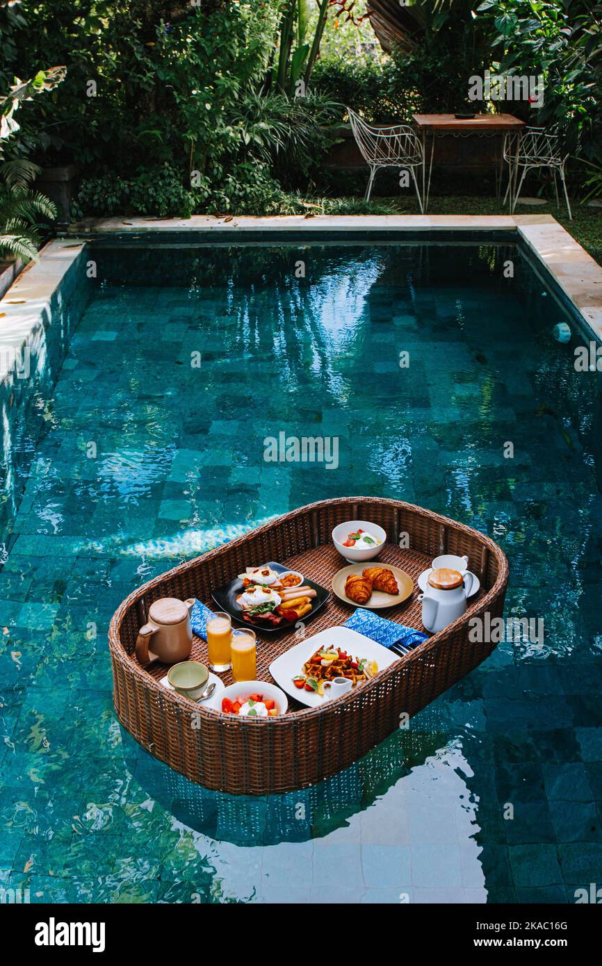 Le plateau de petit-déjeuner en rotin synthétique flotte au milieu de la piscine Banque D'Images