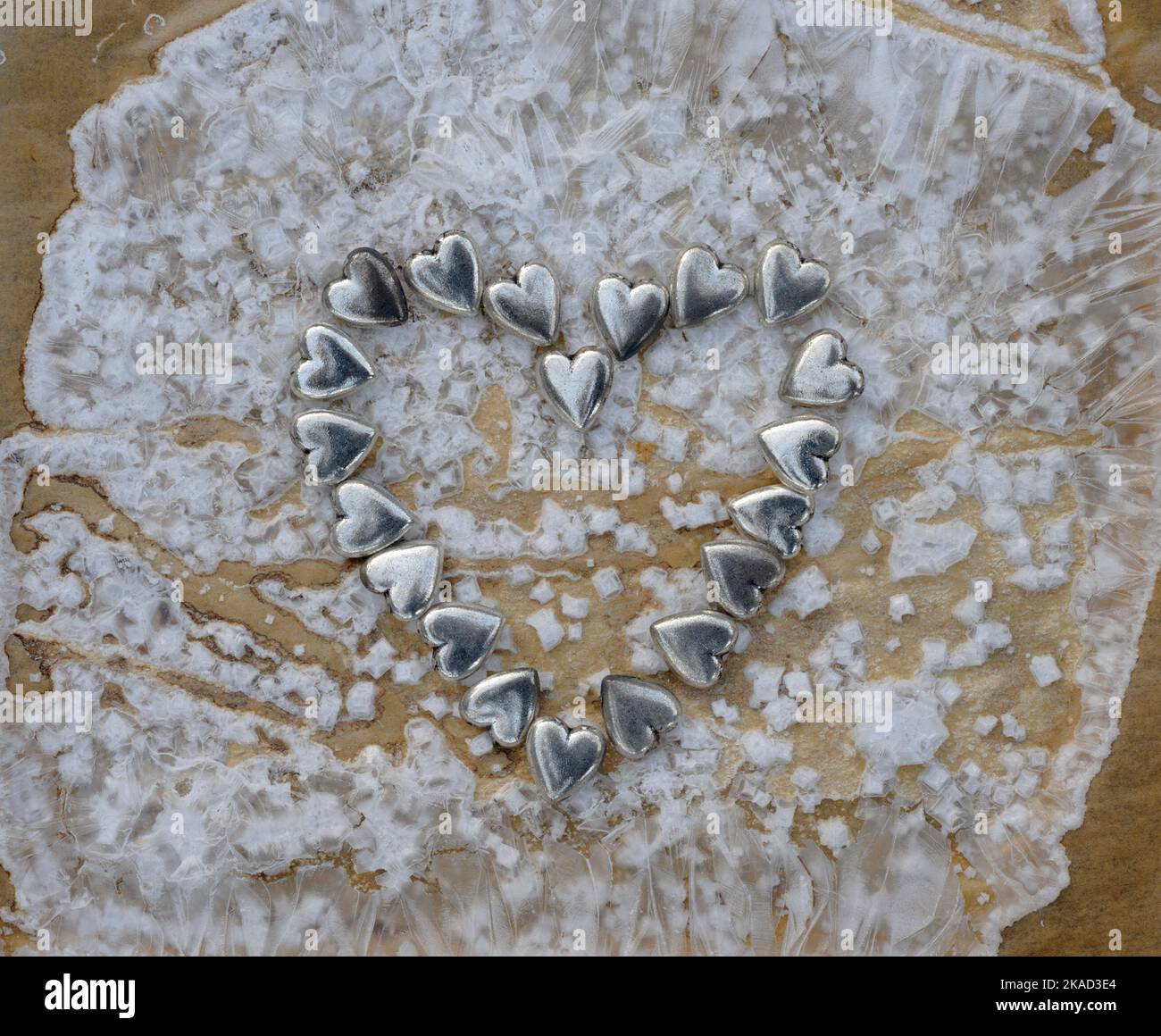 Arrangement de 20 petits coeurs métalliques pour créer une grande forme de coeur, sur fond de cristaux de sel de mer formés quand la saumure sèche, sur le dos de brun Banque D'Images