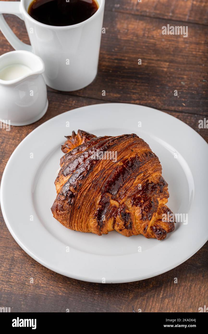 Croissant avec café à côté sur une table en bois Banque D'Images