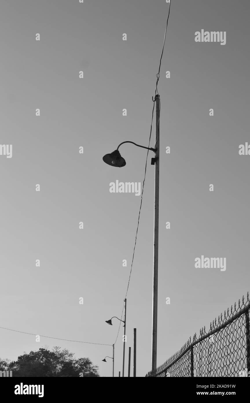 Photo en niveaux de gris d'une rangée de réverbères avec une clôture barbelée en arrière-plan Banque D'Images