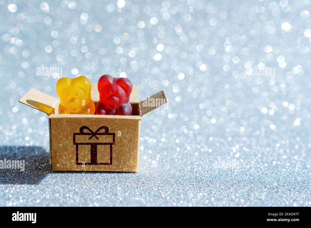 Mélange de bonbons colorés en forme d'ours en gélatine dans une boîte cadeau en carton isolée sur un fond étincelant. Banque D'Images
