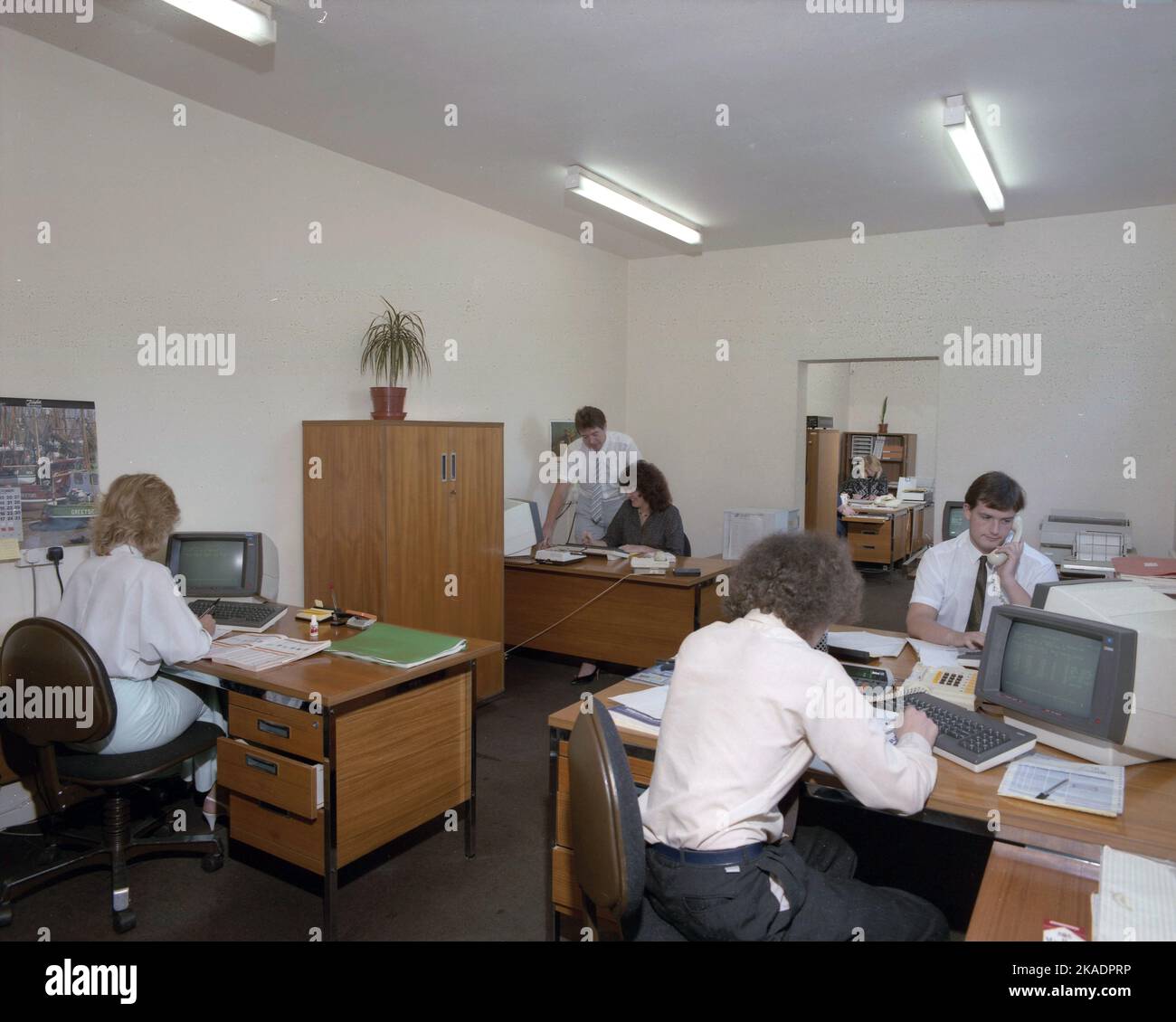 1989, personnel historique, masculin et féminin dans un bureau ouvert, assis à des bureaux en bois, travaillant avec les petits terminaux d'ordinateur de l'époque, Angleterre, Royaume-Uni. Banque D'Images