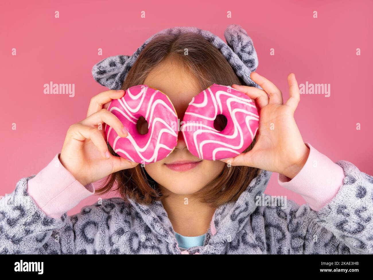 fille en kigurumi ou en pyjama avec des beignes à la place des yeux sur un fond rose. Photo de haute qualité Banque D'Images