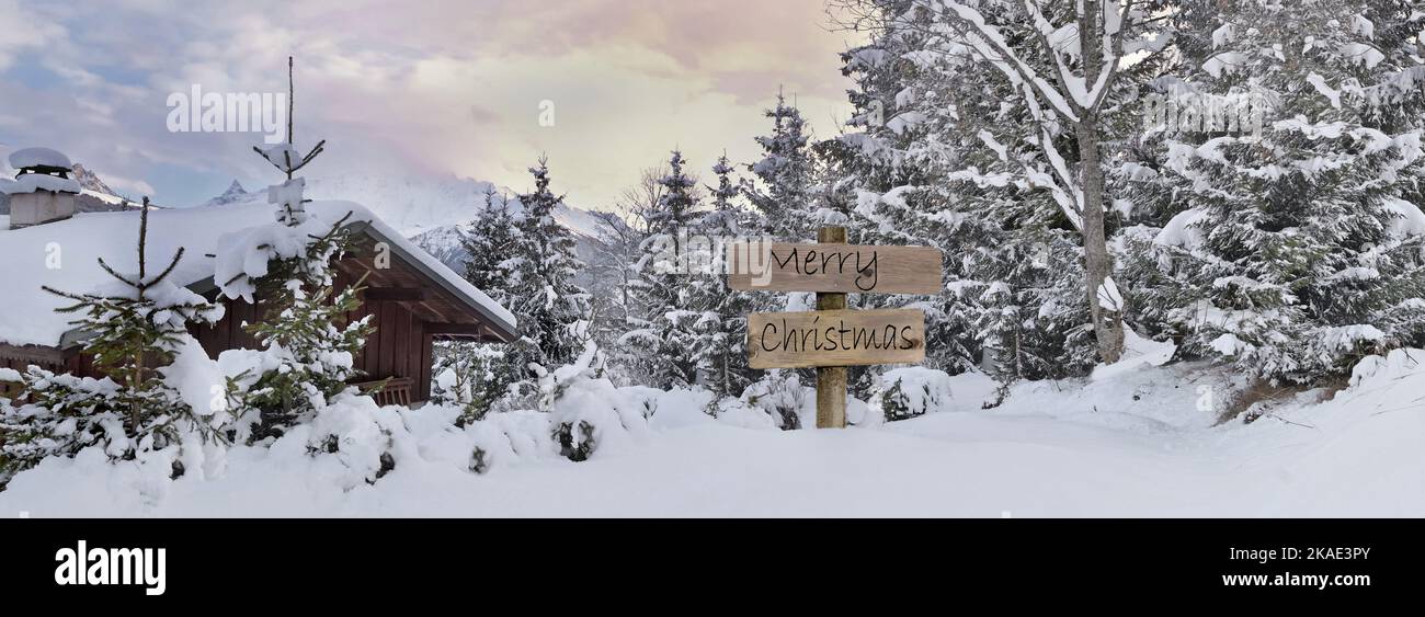 joyeux noël écrit sur une affiche en bois à côté d'un chalet alpin et d'une forêt dans la neige Banque D'Images