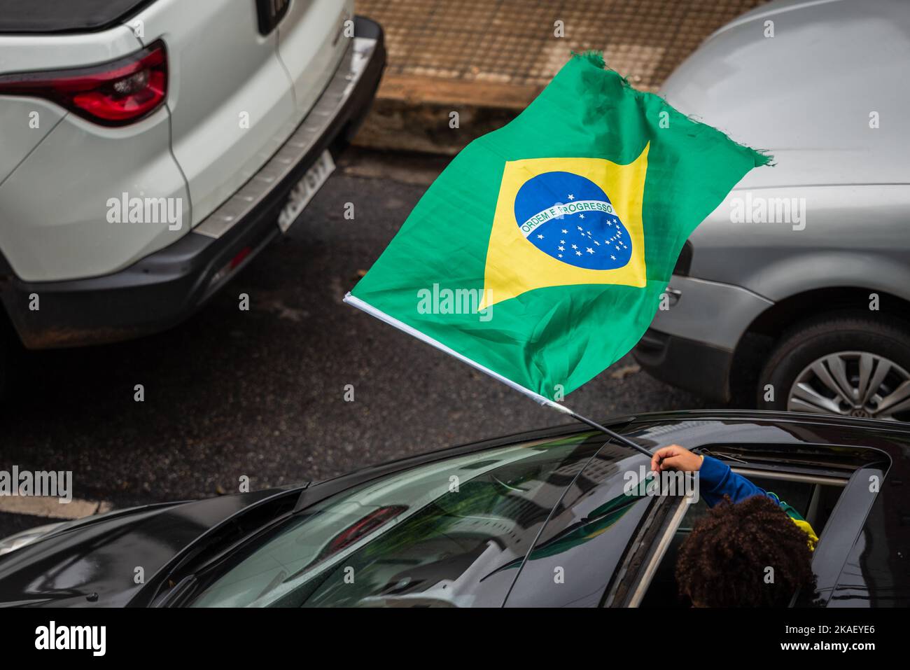 Jeune fille agitant le drapeau brésilien du toit ouvrant de voiture à Belo Horizonte, Brésil. Banque D'Images