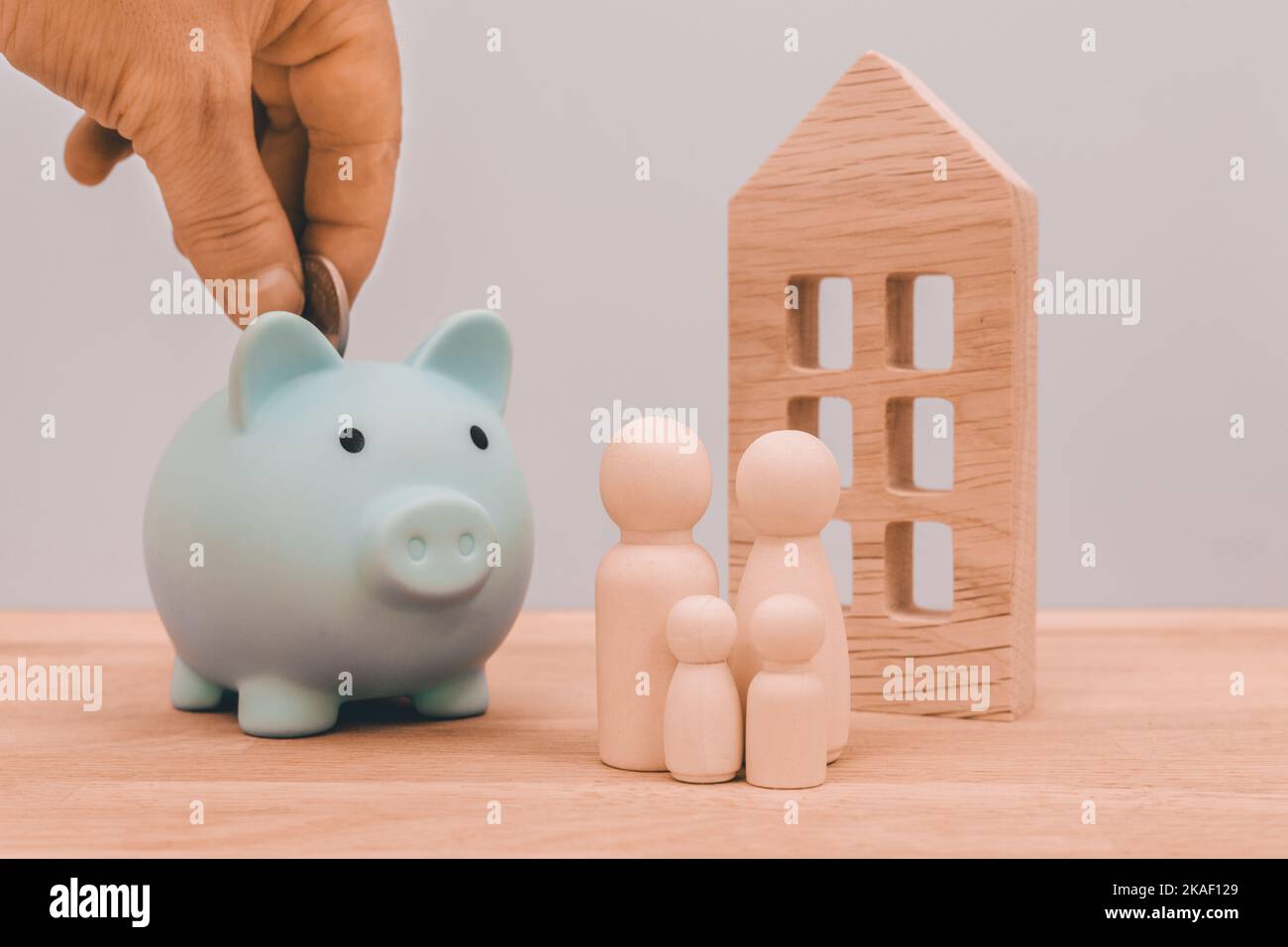 Économiser pour une maison de rêve, concept d'affaires et d'investissement, jeter à la main des pièces dans une banque de piggy, figurines en bois d'une famille avec des enfants et un confortable Banque D'Images