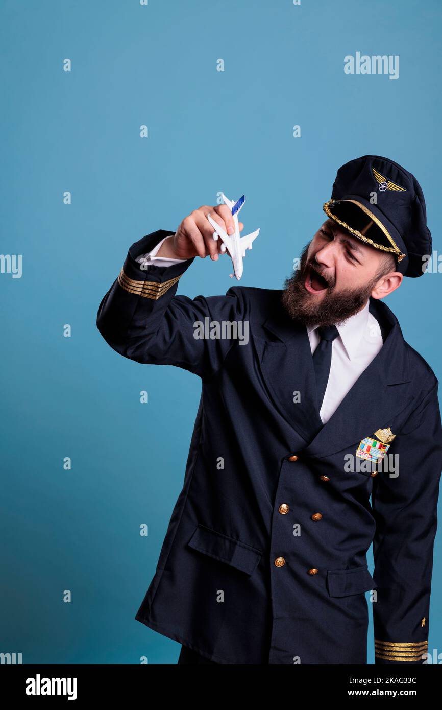 Aviateur souriant en uniforme tenant un modèle d'avion, capitaine de l'académie d'aviation jouant avec l'avion. Personne de l'équipage de l'avion regardant un jouet à jet commercial, vue latérale studio vue moyenne Banque D'Images