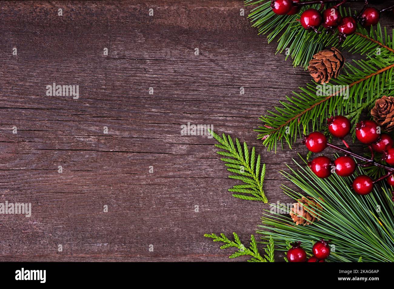 Bordure latérale de Noël avec branches à feuilles persistantes, baies rouges et cônes de pin. Vue en hauteur sur un arrière-plan en bois sombre avec espace de copie. Banque D'Images