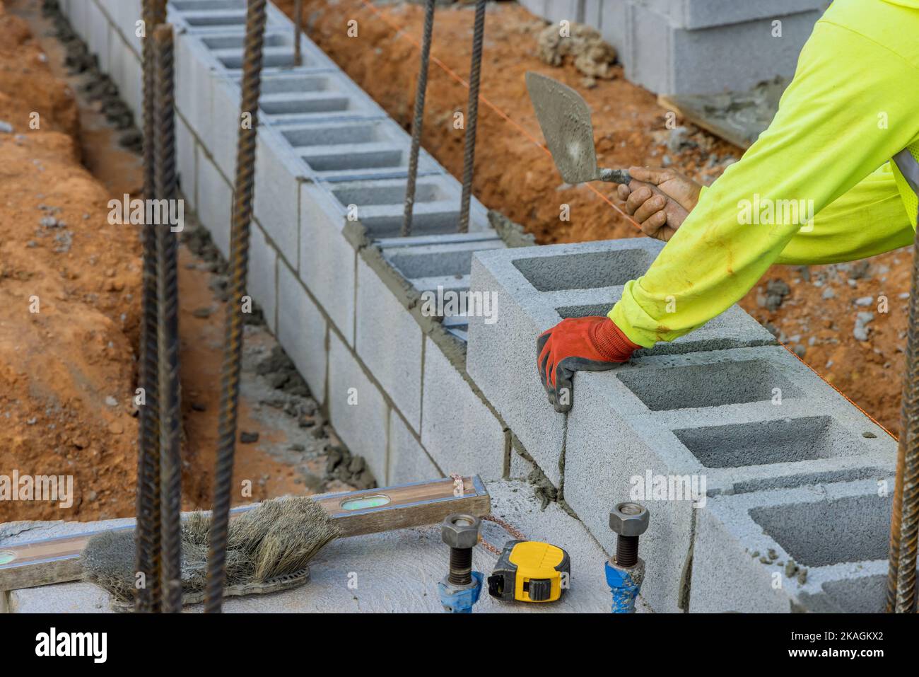 Bricklayer ouvrier de construction mettant en place une autre rangée de blocs de ciment dans le chantier de construction Banque D'Images