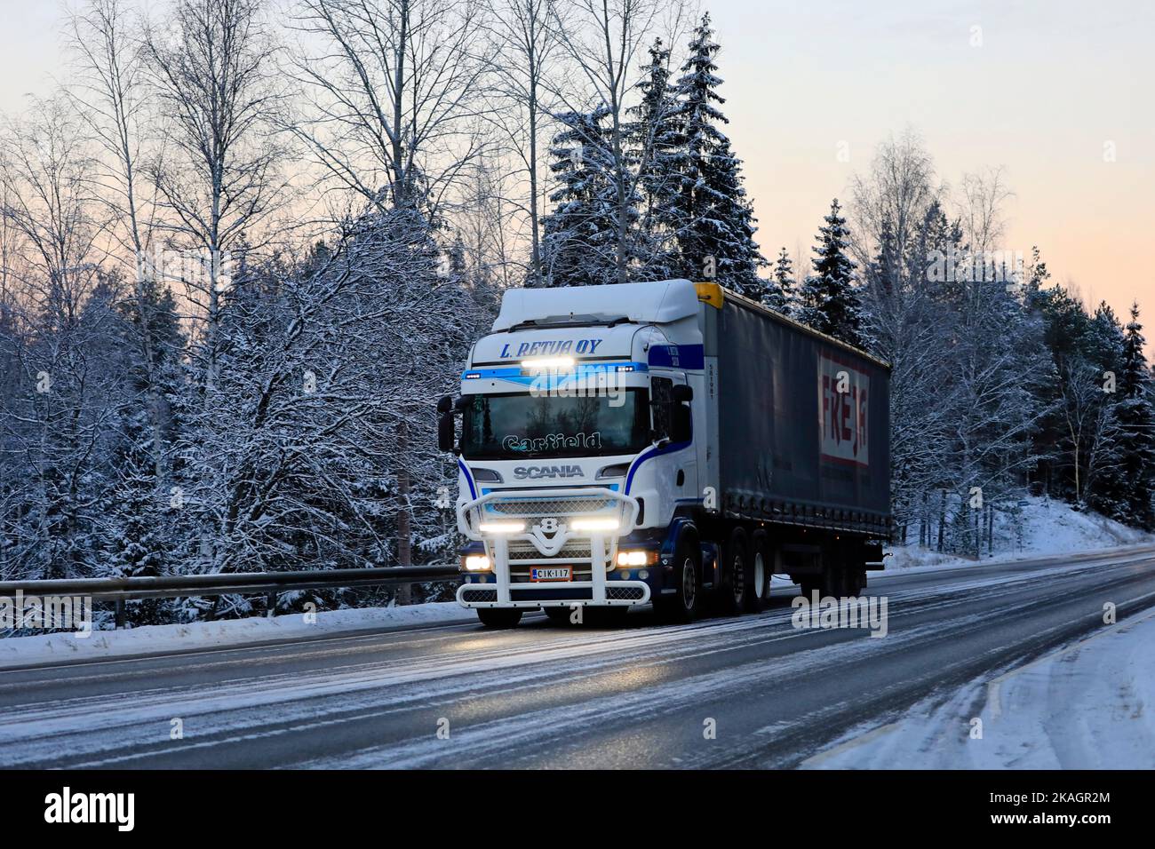 Le camion personnalisé Scania L Retva Oy tire la semi-remorque sur l'autoroute 52 au crépuscule en hiver, les feux de route s'allument brièvement. Salo, Finlande. 27 décembre 2021. Banque D'Images