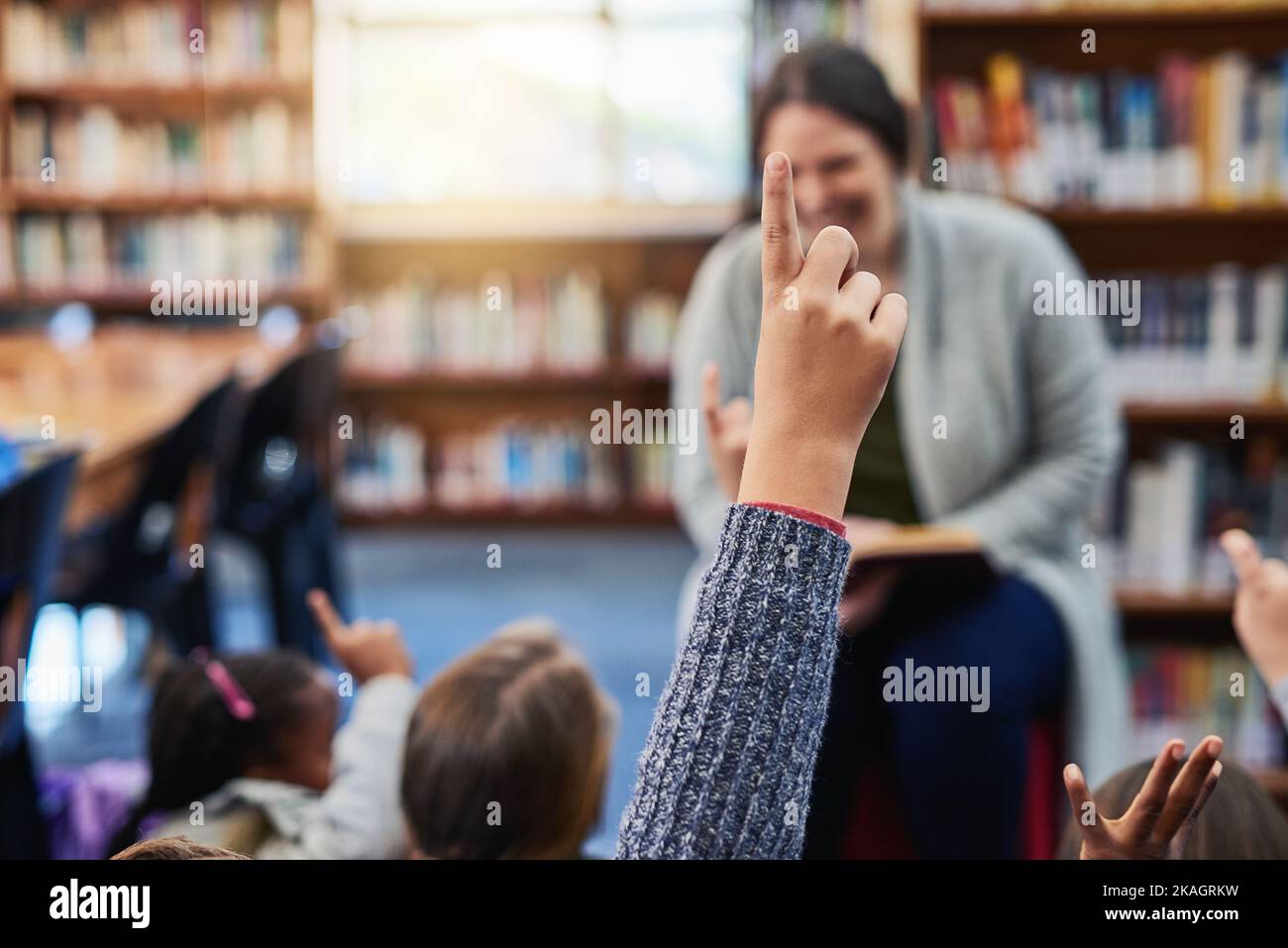 Les enfants ont beaucoup de questions qui alimentent leurs esprits curieux. Un garçon de l'école primaire levant la main à son professeur dans la bibliothèque. Banque D'Images