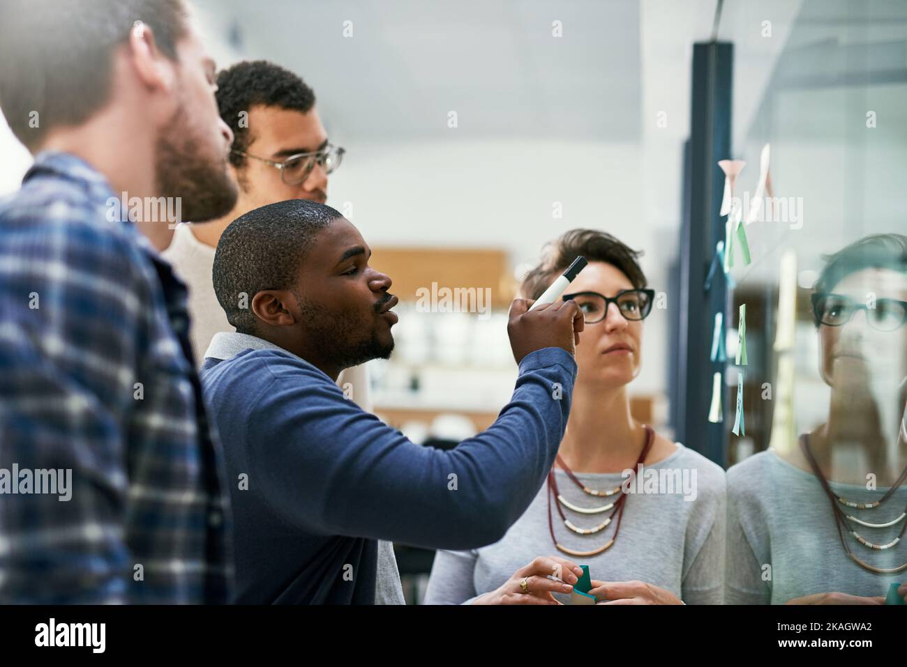 Mettre de grands plans en place puis en action. Un groupe de concepteurs remue-méninges avec des notes sur un mur de verre dans un bureau. Banque D'Images