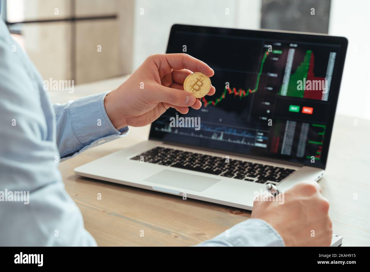 Gros plan sans visage d'un investisseur professionnel masculin détenant du bitcoin, utilisant un ordinateur portable avec un diagramme de la bourse de négociation, investissant dans la crypto-monnaie à son bureau. Investissement et technologie Banque D'Images