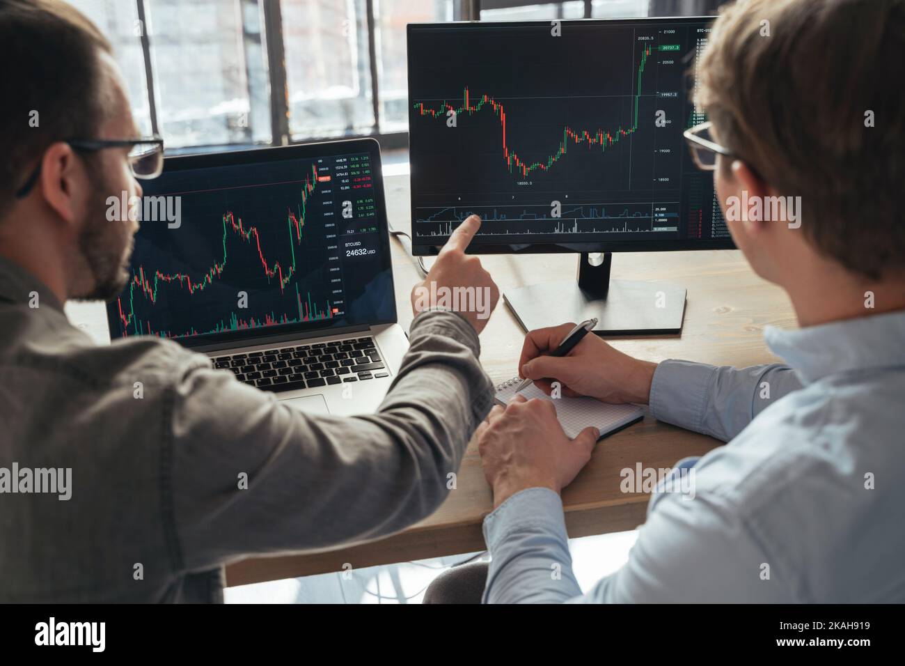 Gros plan de deux hommes crypto commerçants assis à la table de bureau ensemble devant le pc, le suivi des diagrammes de données des stocks à l'écran, l'analyse des flux de prix. Travail d'équipe à but lucratif. Argent numérique Banque D'Images