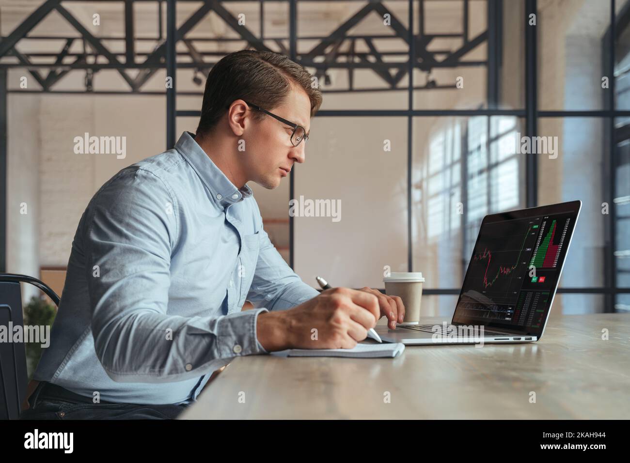 Homme occupé commerçant de lunettes travaillant en ligne sur ordinateur portable à son bureau, crypto-expert financier analyse graphique regardant l'écran de moniteur avec le diagramme, écrivant dans le bloc-notes. Crypto-monnaie Banque D'Images