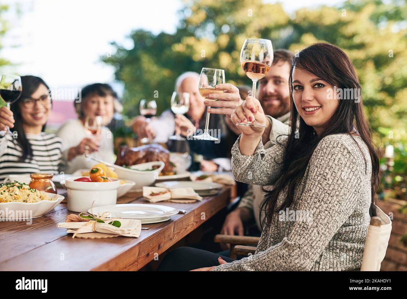 La famille est à nouveau ensemble. Un groupe de personnes gaies qui élèvent leurs verres à vin pour griller sur une table à manger tout en regardant l'appareil photo. Banque D'Images