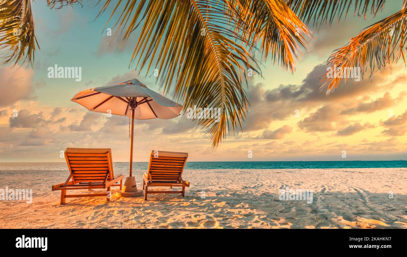 Belle plage tropicale panoramique. Coucher de soleil été paysage de l'île avec amour couple chaises parapluie paume feuilles calme mer rivage, côte. Voyage romantique Banque D'Images