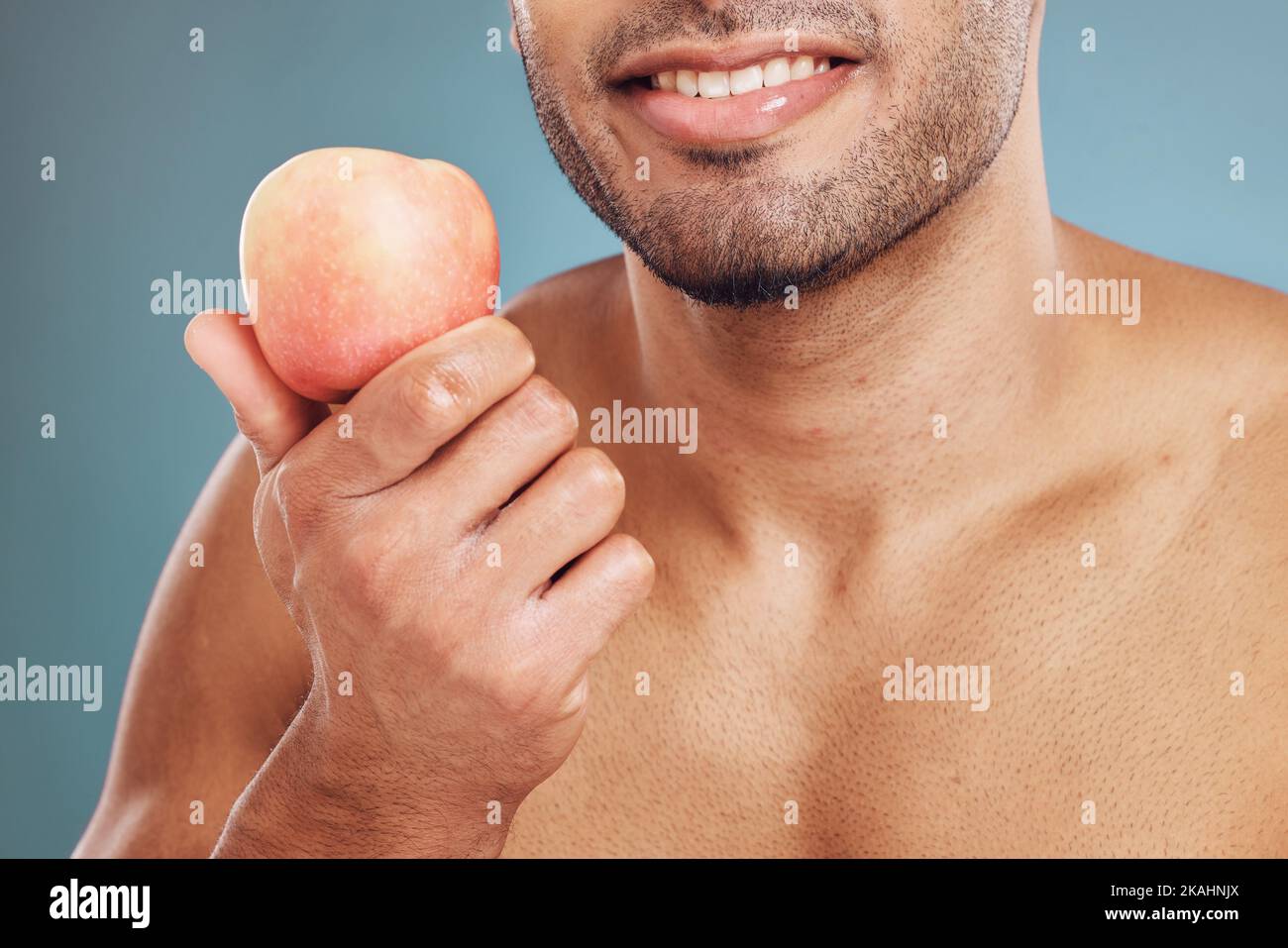 Main, pomme et beauté avec un modèle d'homme en studio sur un fond bleu pour la santé manger ou le régime. Nourriture, fruits et santé avec un jeune homme posant avec Banque D'Images