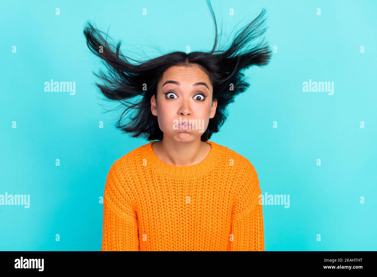 Photo de fille impressionnée funky vêtue orange Pullover fleurs joues air soufflage isolé teal couleur fond Banque D'Images