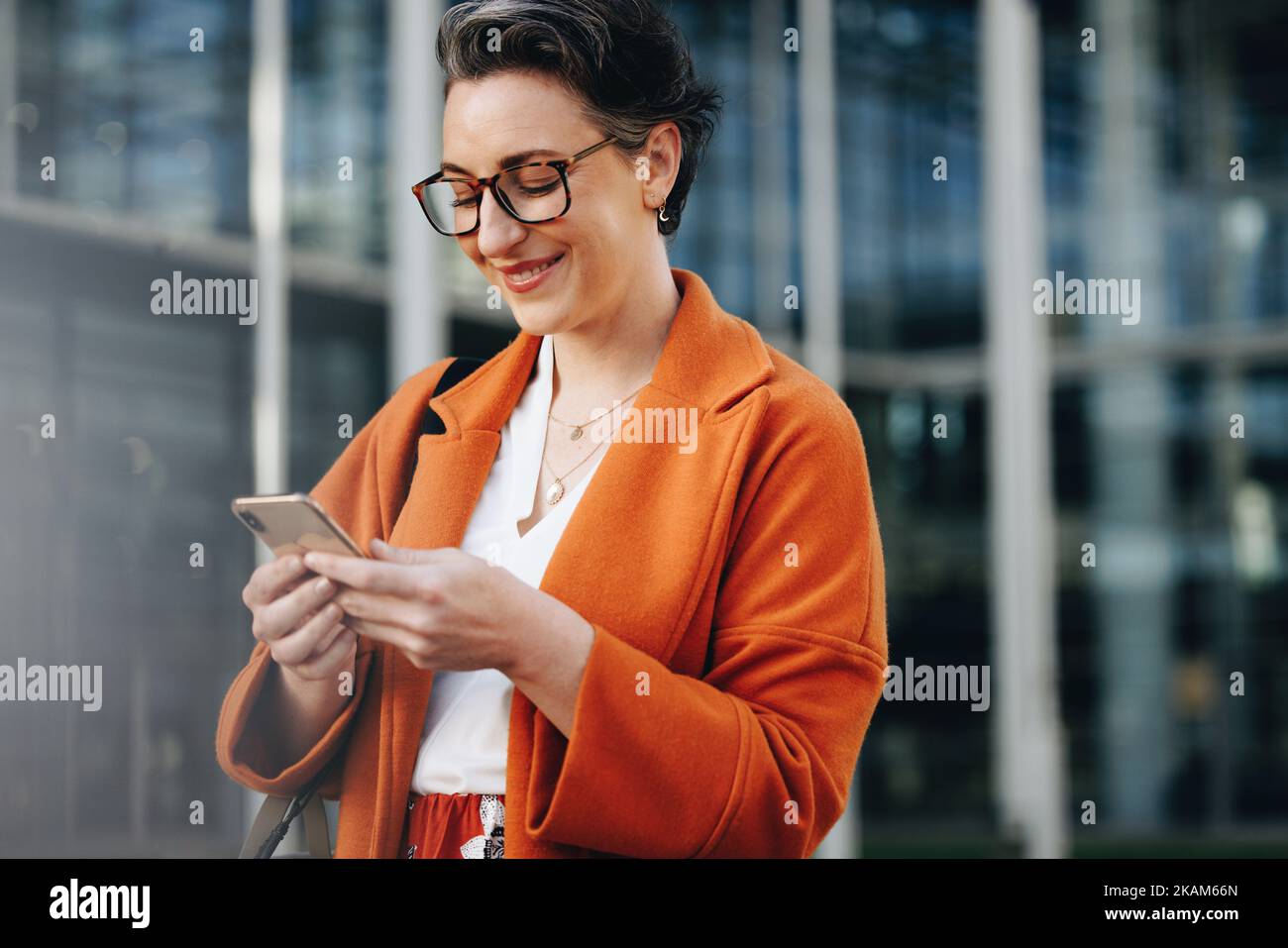 Une heureuse femme d'affaires souriant sur son smartphone tout en se rendant au travail en ville. Femme d'affaires mûre lisant un message texte sur son chemin à l'extérieur Banque D'Images