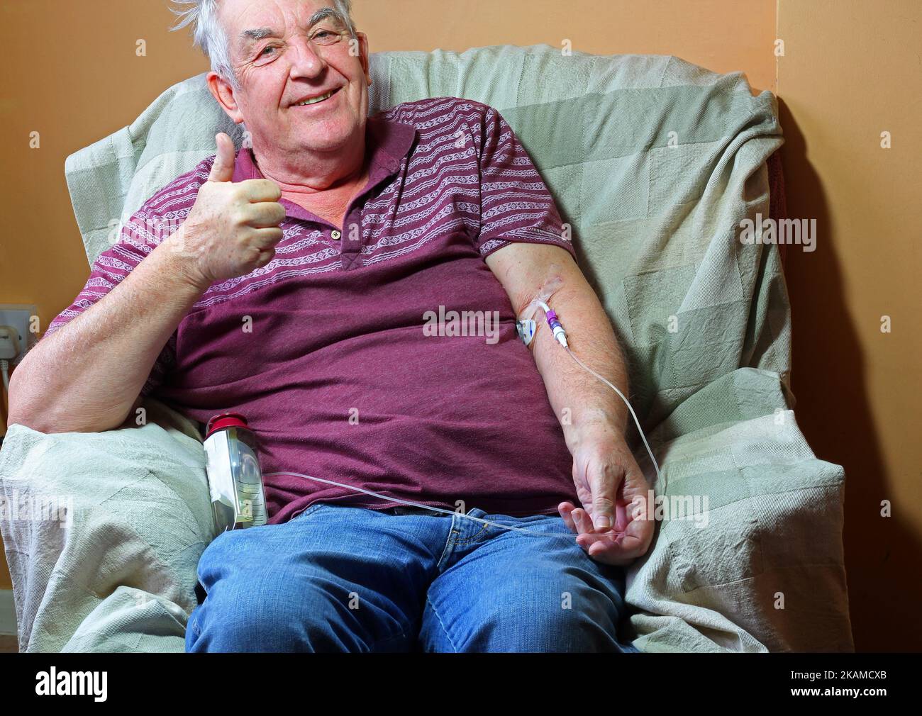 Homme âgé ou âgé assis dans une chaise à la maison et recevant une chimiothérapie. Par une ligne pic dans sa veine. L'homme a le cancer. Banque D'Images