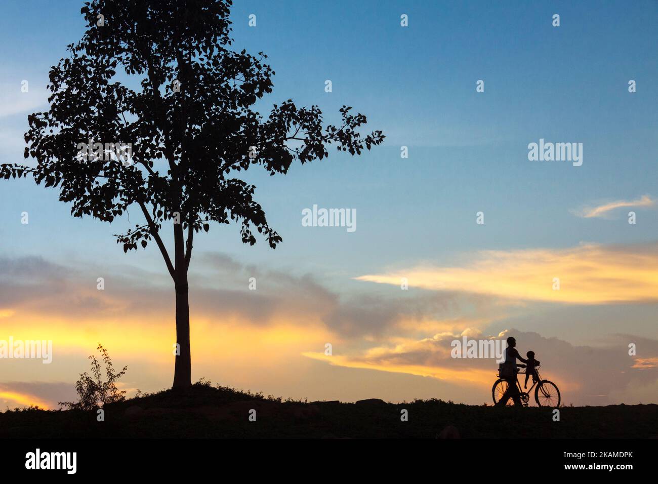 Khajuraho, Madhya Pradesh, Inde : UN homme et un petit enfant prennent une balade idyllique à vélo au coucher du soleil. Banque D'Images