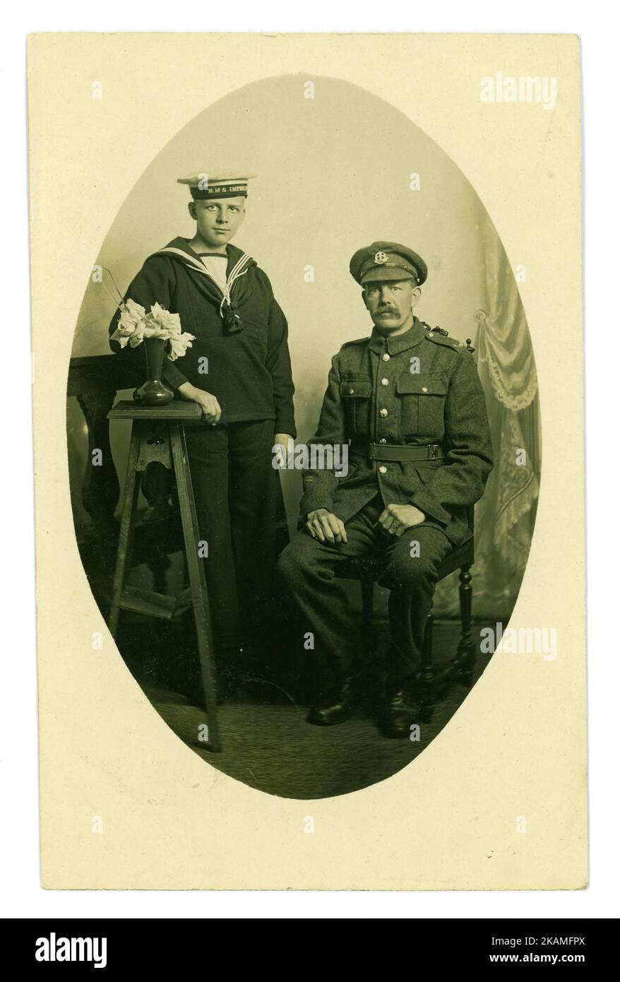 Portrait de père et de fils en studio de carte postale datant de WW1. Le père est avec le Middlesex Regiment (insigne sur le cap) et le fils est un cadet naval sur le HMS impénétrables, un navire d'entraînement (HMS impénétrables sur le cap), Middlesex, S.E. Angleterre près de Londres, vers 1916 Banque D'Images
