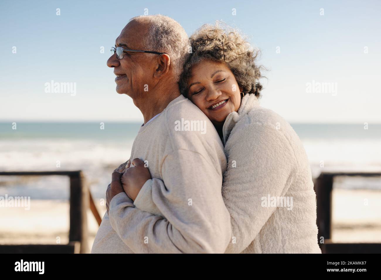 Affectueuse femme âgée souriant avec joie tout en embrassant son mari au bord de l'océan. Couple romantique de personnes âgées appréciant passer un certain temps de qualité togeth Banque D'Images