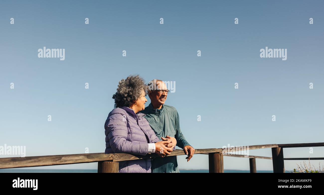 Couple de personnes âgées heureux ayant une discussion joyeuse tout en obtenant une vue rafraîchissante sur un pont de pied en bois. Couple senior romantique appréciant une plage relaxante Banque D'Images