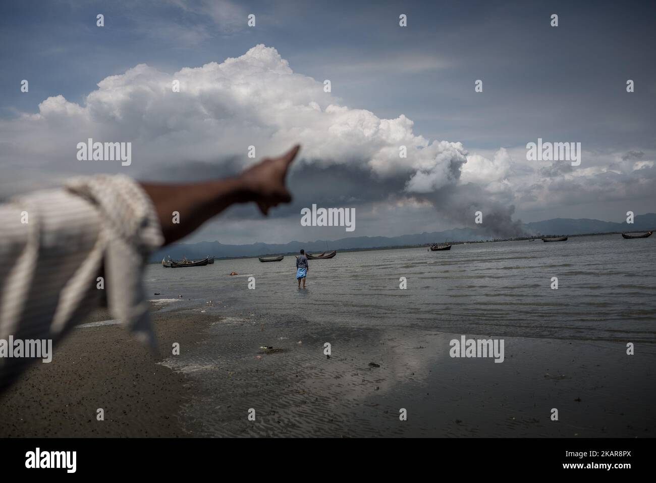 Pointant du doigt, un réfugié de Rohingya fume du côté de la frontière birmane alors que l'armée du Myanmar met le feu sur son village. Shahpirer DIP, Teknaf, Bangladesh ; 14 septembre 2017. Le Bangladesh utilisera des troupes pour fournir une aide étrangère à la ville frontalière submergée par les réfugiés musulmans Rohingya du Myanmar, ont annoncé à la fin du 14 septembre. Cette décision fait suite à la critique des conditions chaotiques dans lesquelles les secours ont été distribués dans les immenses camps autour de Cox's Bazar, où environ 389 000 Rohingya de l'État Rakhine du Myanmar sont arrivés depuis 25 août. (Photo par Banque D'Images