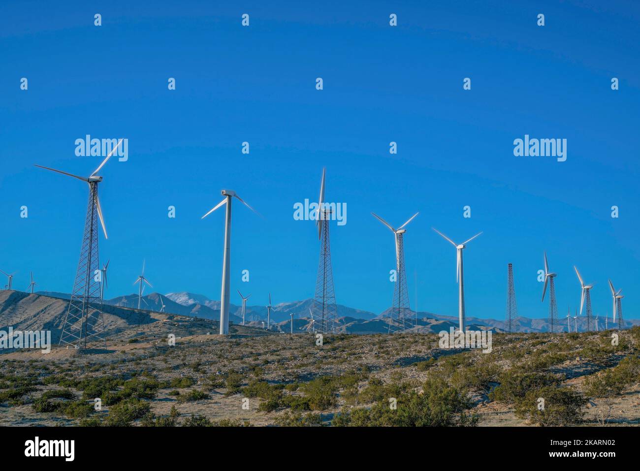 Éoliennes avec tours en treillis et en acier tubulaire sur un désert avec des arbustes sauvages en Californie. Moulins à vent au sommet d'une chaîne de montagnes contre le bleu Banque D'Images