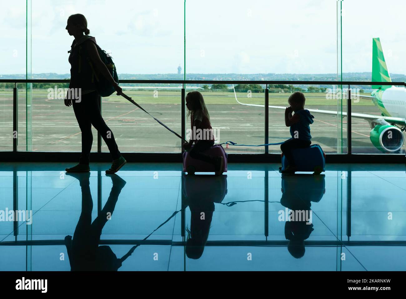 Dans la salle de transit de l'aéroport, la jeune mère porte des valises, les petits enfants jusqu'à la porte d'embarquement pour embarquer dans un avion. Un mode de vie familial actif, un voyage Banque D'Images