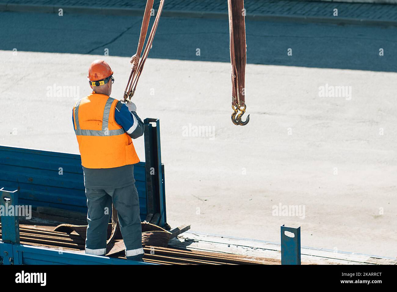 Le déflecteur du casque et de la veste décharge les tuyaux et raccords métalliques de la caisse du camion par temps clair. Arrière-plan de production. Flux de travail authentique sur site de construction. Le déflecteur au travail. Banque D'Images